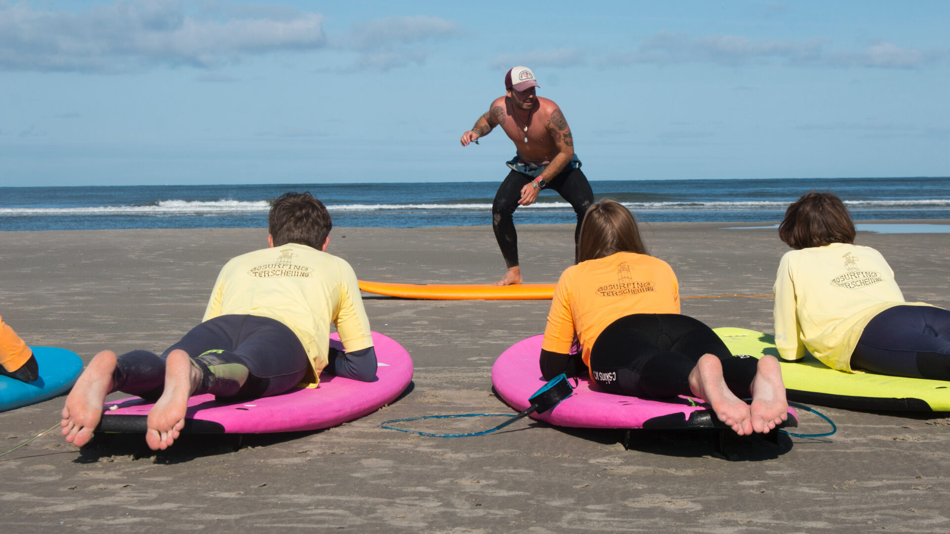 Leerlingen liggen op hun surfplank op het strand